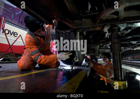 Two mechanics fitting snow chains to a bus wheel using a bus garage inspection pit. Stock Photo