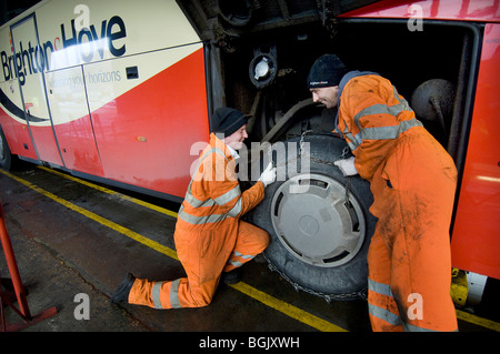 Two mechanics fitting snow chains to a bus wheel using a bus garage inspection pit. Stock Photo