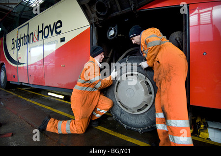 Two mechanics fitting snow chains to a bus wheel using a bus garage inspection pit. Stock Photo