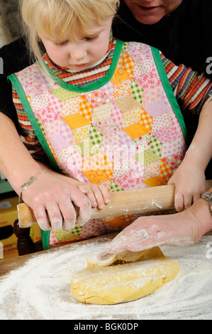 Stock photo of a four year old girl using a rolling pin to flatten the cookie mixture before she makes some biscuits. Stock Photo