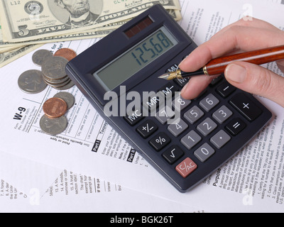 Female hand calculating taxes on calculator with W-9 income tax forms underneath Stock Photo