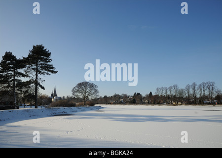 Three spires cathedral and frozen Stowe Pool with fir trees and shadows on snowy winter’s day 2010 Lichfield England Stock Photo