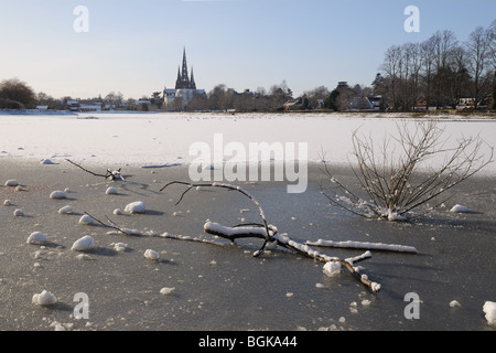 Three spires cathedral and frozen Stowe Pool with fallen wood on the ice on snowy winter’s day 2010 Lichfield England Stock Photo