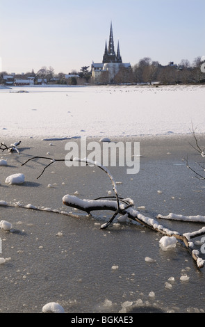 Three spires cathedral and frozen Stowe Pool with fallen wood on the ice on snowy winter’s day 2010 Lichfield England Stock Photo