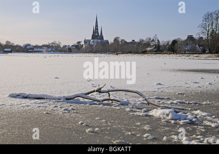 Three spires cathedral and frozen Stowe Pool with fallen wood on the ice on snowy winter’s day 2010 Lichfield England Stock Photo