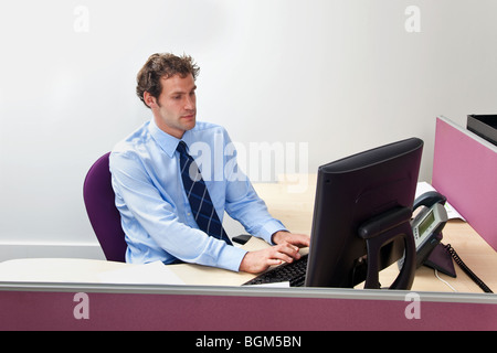 A male office worker sat at his desk working on a computer Stock Photo