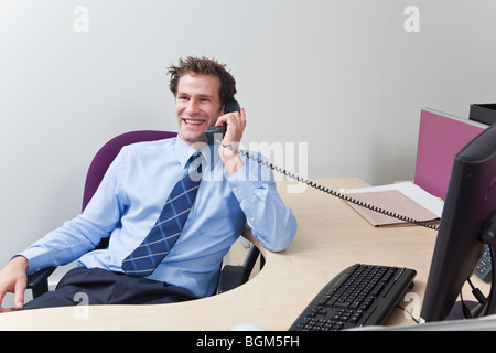 A businessman wearing shirt and tie sat at his desk chatting on the telephone. Stock Photo