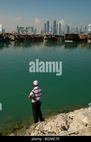Fisherman on the Corniche quayside with Doha, Qatar with skyscrapers and traditional dhow fishing boats in background Stock Photo