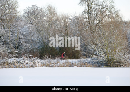 A couple walk past an ice covered lake on a snowy cold wintery day in Redditch Worcestershire England uk Stock Photo