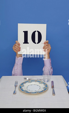 man eating at table holds up 10 sign to rate dinner