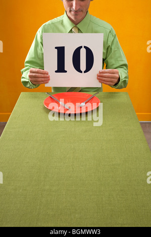 man eating at table holds up 10 sign to rate dinner Stock Photo