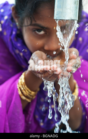 Indian girl drinking from a water pump. India Stock Photo