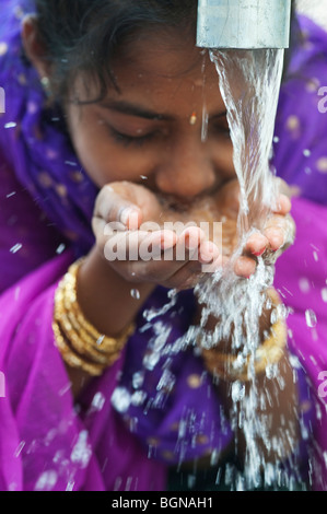 Indian girl drinking from a water pump. India Stock Photo