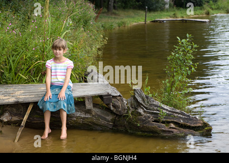 little cute girl sitting on bridge near river Stock Photo