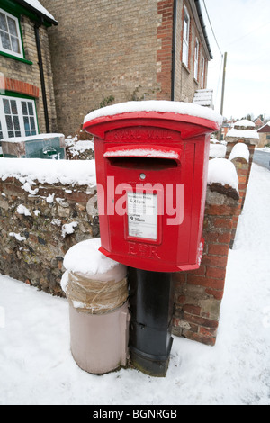 Red postbox covered with snow in winter, Ashley village near Newmarket, Cambridgeshire UK Stock Photo