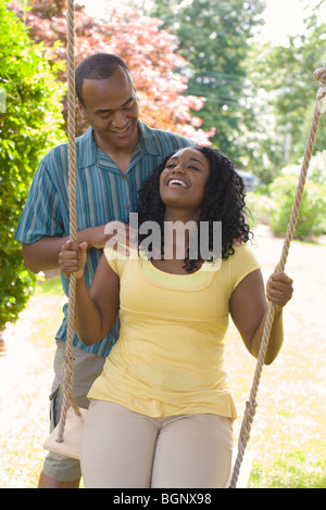 Young woman sitting on a swing and a mid adult man standing behind her Stock Photo
