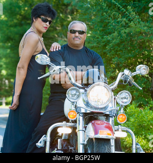 Senior man sitting on a motorcycle with a mature woman standing beside him Stock Photo