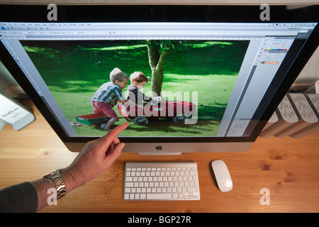 Apple iMac 27' computer on home office desk with external hard drives, wireless keyboard and mouse - hand pointing Stock Photo