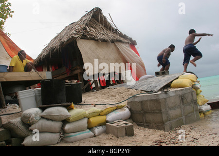 A family living next to the sea, on Pacific island of Kiribati, re-enforce their property with a sea wall made of sandbags. Stock Photo