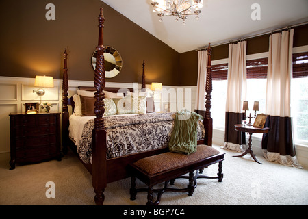 Master bedroom with king size four poster bed covered with matching fabric duvet and stack of pillows. Cabinets on the side Stock Photo