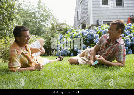 Side profile of a mature man with his brother lying on grass and holding table tennis rackets Stock Photo