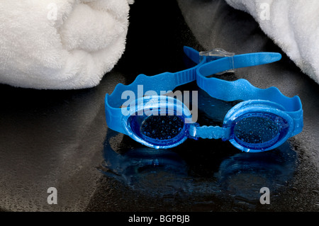 Wet swimming goggles and towels on a reflective surface Stock Photo