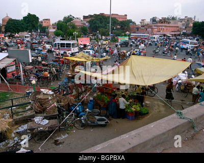 Jaipur traffic at cross roads, with vegetable vendors under canopy in foreground. Stock Photo