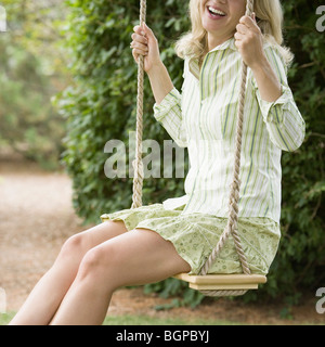 Side profile of a mature woman swinging on a rope swing and smiling Stock Photo