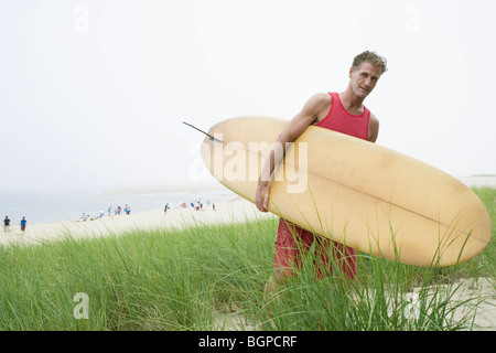 Mature man carrying a surfboard on the beach Stock Photo