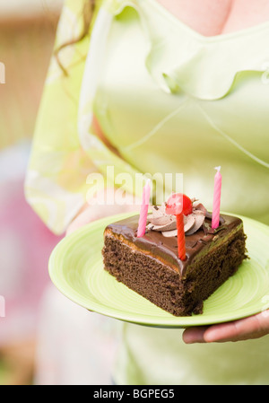 Mid section view of a woman holding a plate of birthday cake slice Stock Photo