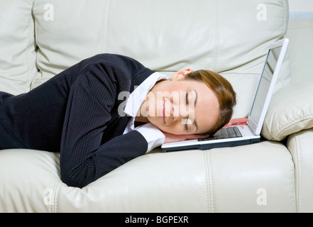 Young business woman with her head on laptop sleeping and dreaming on the couch Stock Photo