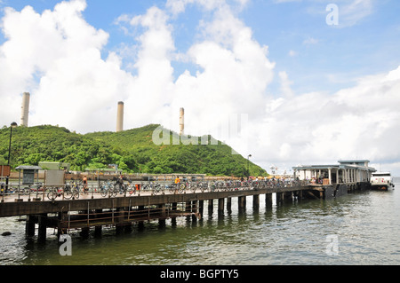 Ferry at the end of the bicycle-lined jetty, looking towards the three stacks of Lamma Power Station, Yung Shue Wan, Hong Kong Stock Photo