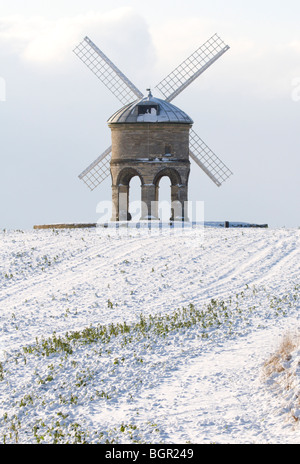 A portrait image of Chesterton Windmill in Warwickshire with snow on the ground and a cloudy sky behind