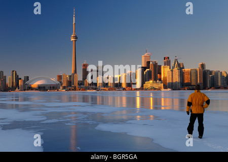 Man standing on frozen Lake Ontario ice looking at Toronto city skyline with golden glow at sunset Stock Photo