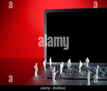 Miniature figures of people standing on keyboard of silver laptop. Clipping path included to drop image into blank screen. Stock Photo
