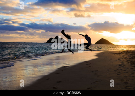 silhouette of twin brothers with drum and guitar leaping in the air at sunrise on a hawaii beach Stock Photo