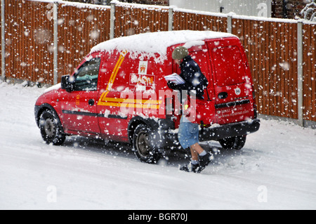 Cold winter weather snowing on Royal Mail delivery postman working from post van in residential street scene in snow storm Brentwood Essex England UK Stock Photo