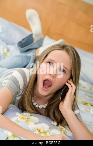 Caucasian preteen girl laying in bed talking on a cell phone and looking very surprised Stock Photo