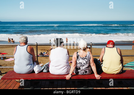 Two mature couples watching surfers on beach in Spain Stock Photo