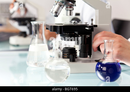 A medical or scientific researcher using a microscope and flasks of liquid in a research laboratory. Stock Photo