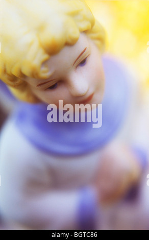 Close up in warm light of childlike angel in white and blue robe with praying hands and warm background Stock Photo