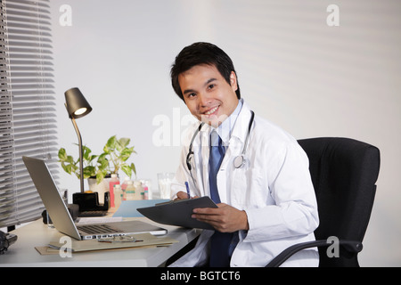 Doctor sitting at desk working on computer, smiling Stock Photo