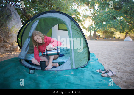 Young woman relaxing in tent pouring a cup of coffee, Van Zyl‚Äôs Pass area, Kaokoland, Namibia Stock Photo