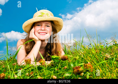 Young teenage girl laying in summer meadow resting chin on hand in straw hat Stock Photo