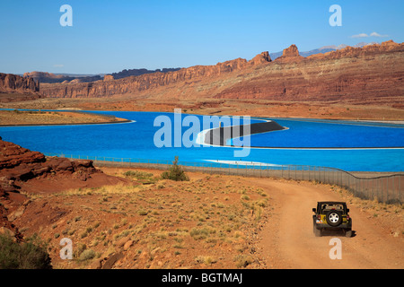 Scene overlooking the bight blue Cane Creek potash mine water evaporation ponds near Moab, Utah, USA and 4x4 truck in foreground Stock Photo