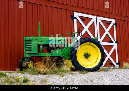 Green vintage John Deere tractor with yellow wheels parked against red barn Stock Photo