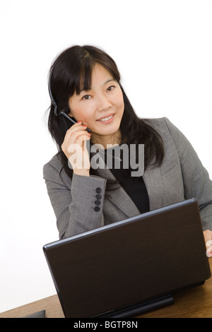 Beautiful Asian Businesswoman working on a laptop computer and talking on a telephone headset. Stock Photo
