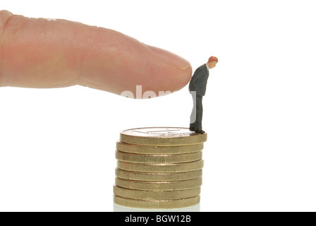 Man's hand pushing a miniature businessman figure from a stack of coins, symbolic image for dismissal Stock Photo