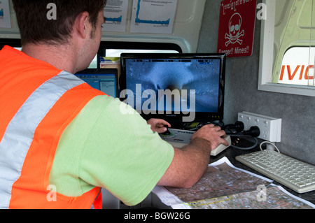 Young man inside van guiding remote video camera through underground pipes looking at live camera footage on screen Stock Photo