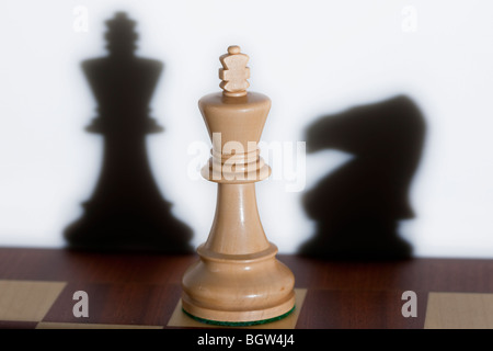 Chess piece - a white king on a chessboard. Shadows from other chess pieces can be seen in the background. Stock Photo